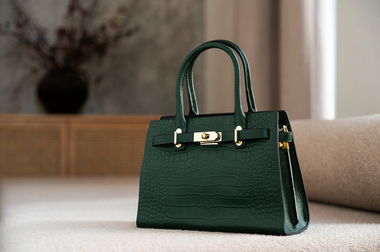 Dark green designer handbag placed on a table in warm well lit room.